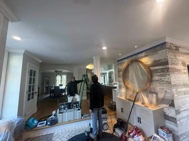Hallway renovation with workers, tools, and a striped accent wall featuring a large round mirror.