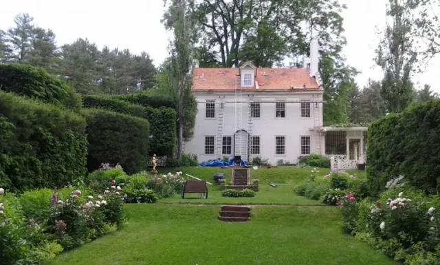 White manor house with a red roof beside a lush formal garden and lawn
