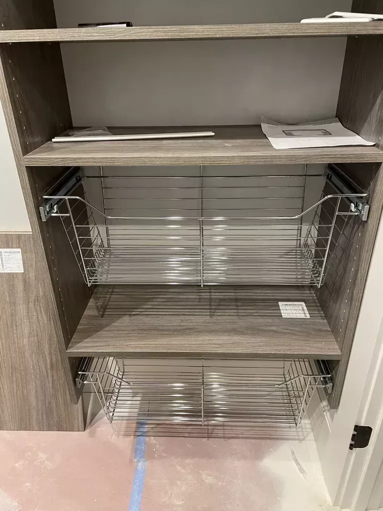 Empty wood cabinet with wire pull-out shelves and a lower drawer in a kitchen or bathroom nook