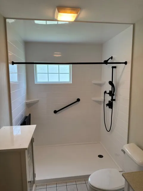 A white walk-in shower with a white base, black fixtures, built-in shelves, and a window.