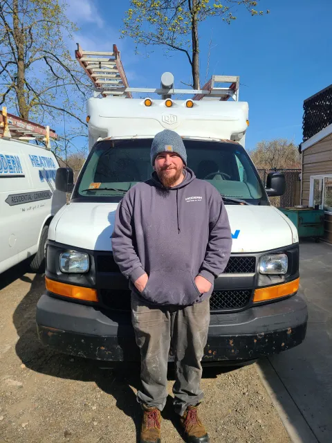 Person in a gray hoodie standing in front of a white utility van on a sunny street.