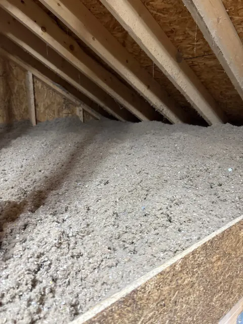 Attic insulation piled beneath exposed wooden rafters and roof decking