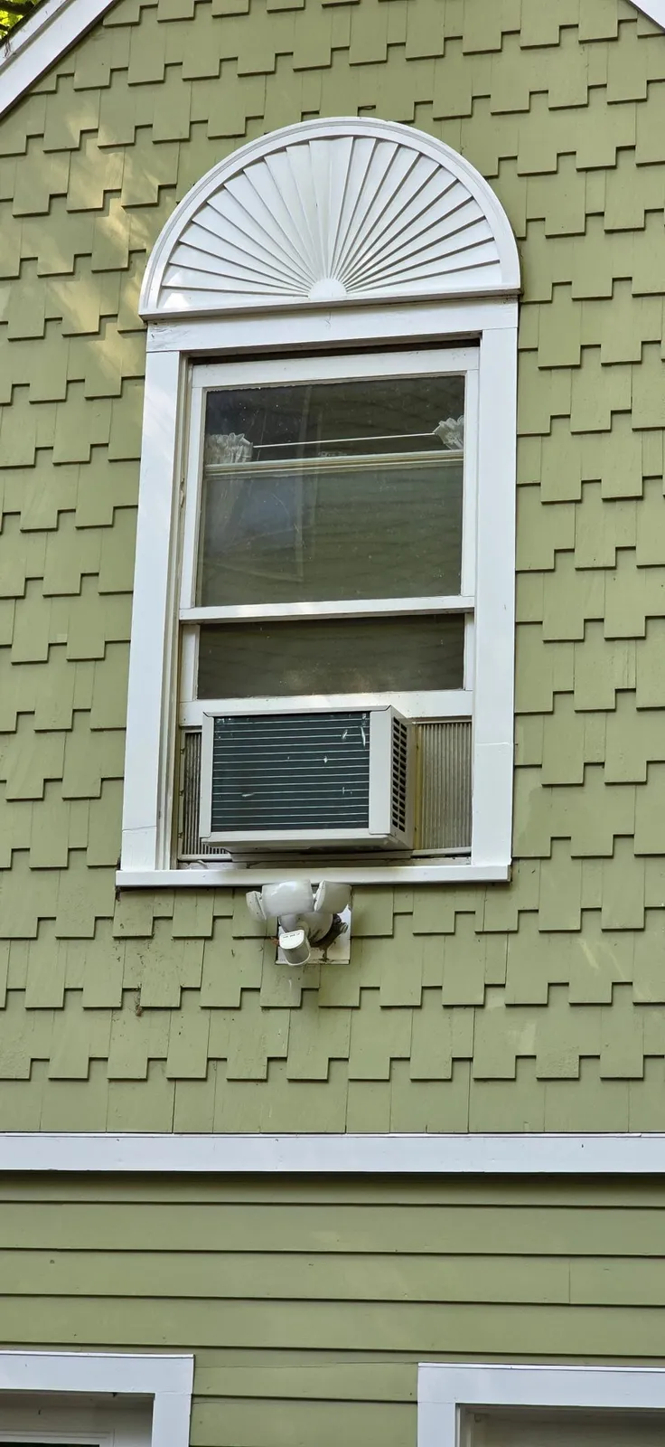 Green shingle house exterior with white window trim, a decorative arch, and a window air conditioner. Expert handyman services in Wellesley, Massachusetts.