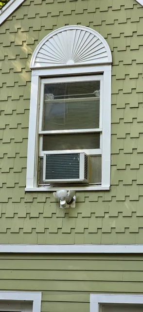 Green shingle house exterior with white window trim, a decorative arch, and a window air conditioner. Expert handyman services in Wellesley, Massachusetts.