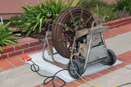 A drain cleaner is sitting on a sidewalk next to a brick wall.