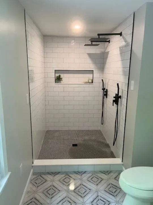 Dreamstate Renovations, LLC - Custom tile shower with sleek white subway tiles, dual showerheads, and geometric tile flooring, showcasing expert craftsmanship in bathroom renovation.