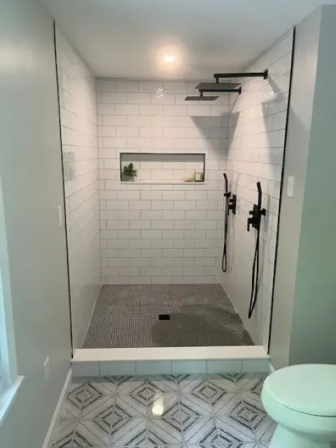 Dreamstate Renovations, LLC - Custom tile shower with sleek white subway tiles, dual showerheads, and geometric tile flooring, showcasing expert craftsmanship in bathroom renovation.