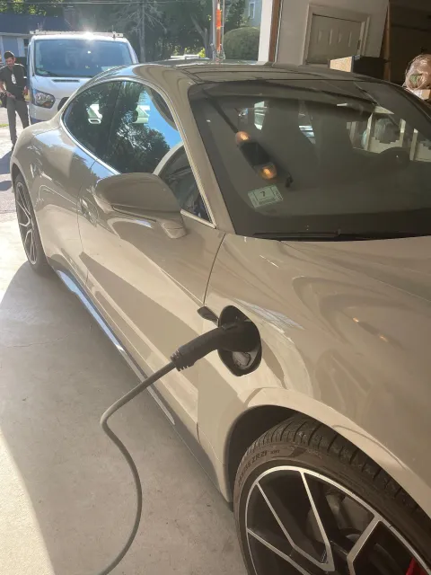 White electric car charging at a station; black charging cable connected to the vehicle.