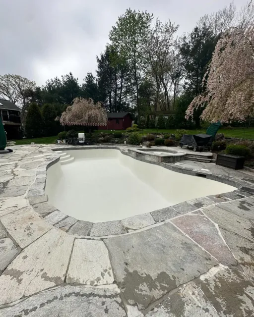 A large white swimming pool surrounded by stone and trees