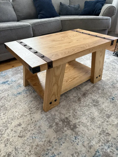 Solid ash coffee table with a lower shelf, blackened steel corner brackets and a leather strap with rivets across the top, styled in a customer's living room