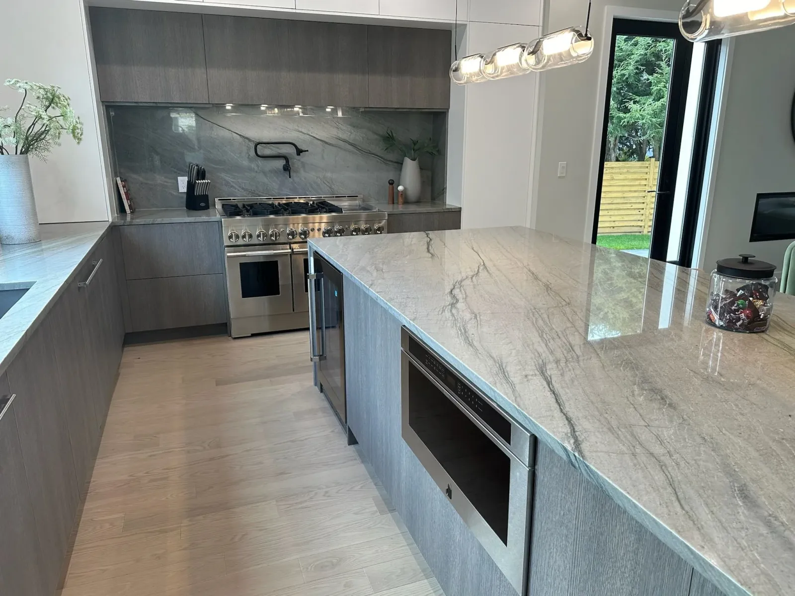 Modern kitchen with gray cabinetry, marble countertops, stainless steel appliances, and pendant lighting.