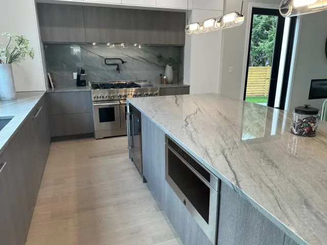 Modern kitchen with gray cabinetry, marble countertops, stainless steel appliances, and pendant lighting.
