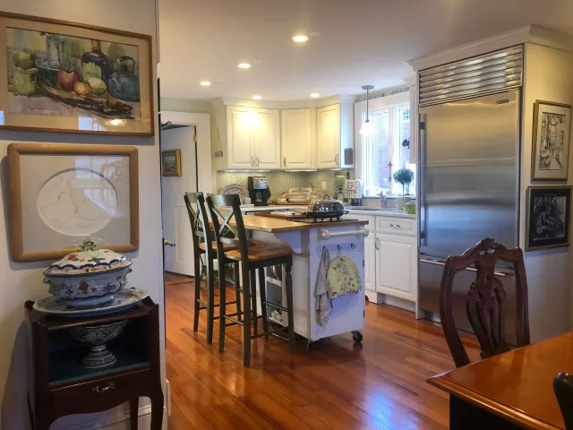 Kitchen with wood floors, white cabinets, island with stools, and stainless steel refrigerator.