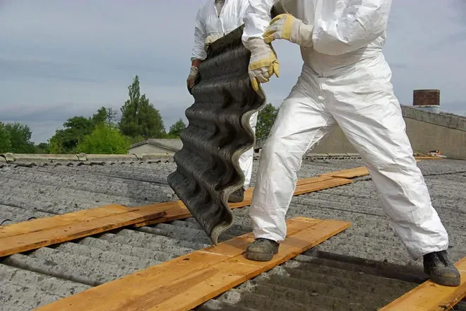 Workers in white suits lifting a large black roofing sheet on a rooftop under construction