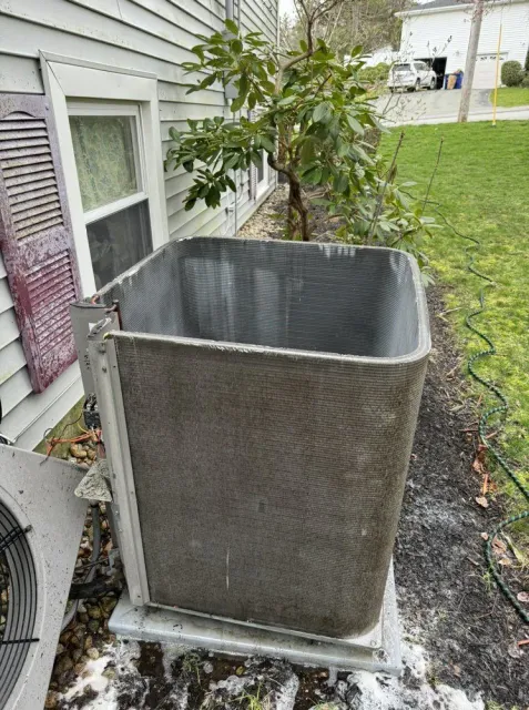An outdoor air conditioning unit with the top half removed sits next to a house.