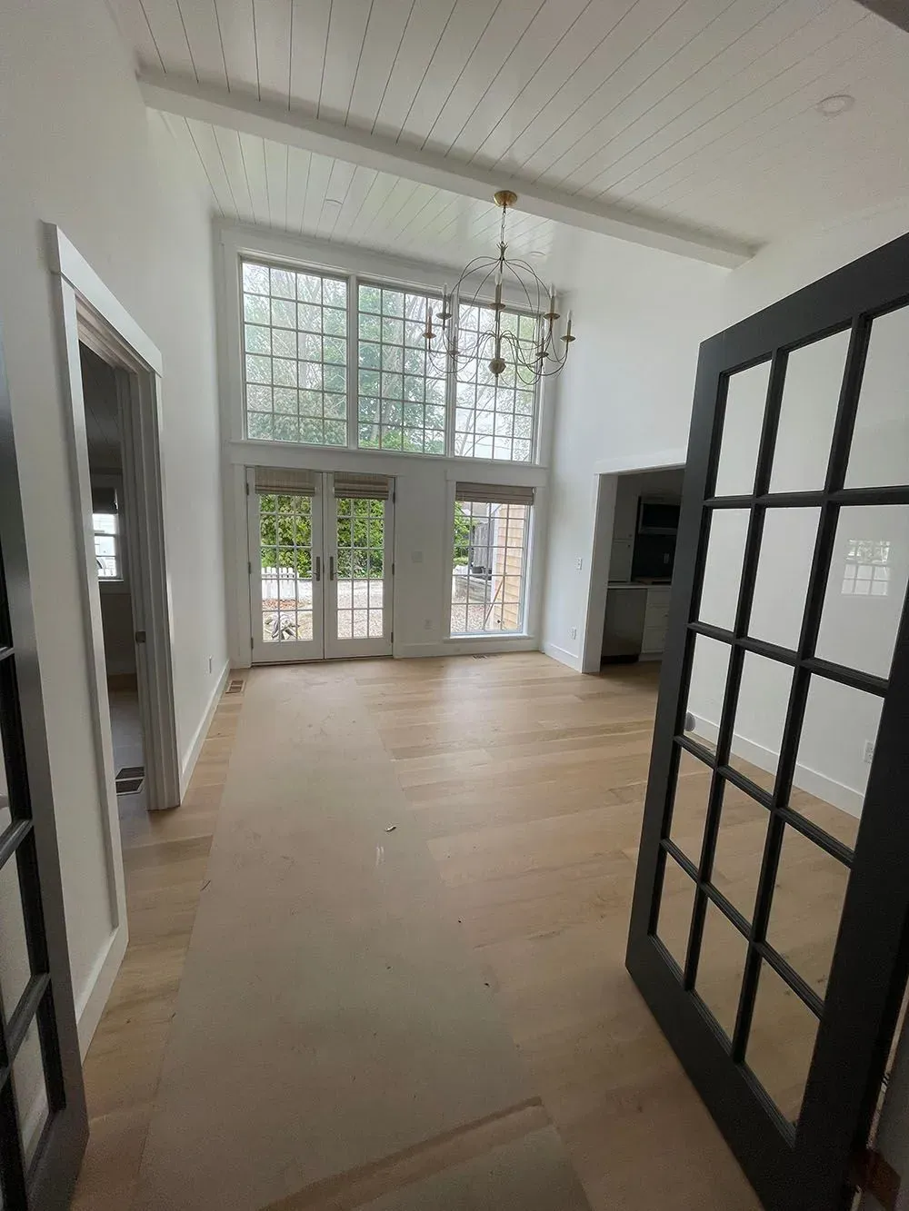 Bright empty room with tall windows, glass doors, and light wood floors