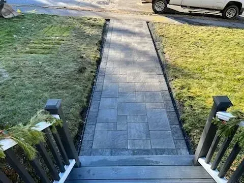 Paver walkway leading from steps to street, bordered by grass. A vehicle is partially visible.