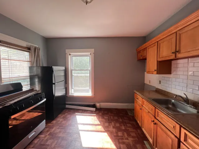 An empty kitchen with wooden cabinets and a black refrigerator