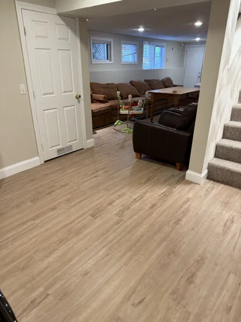 A living room in a basement with hardwood floors and stairs.