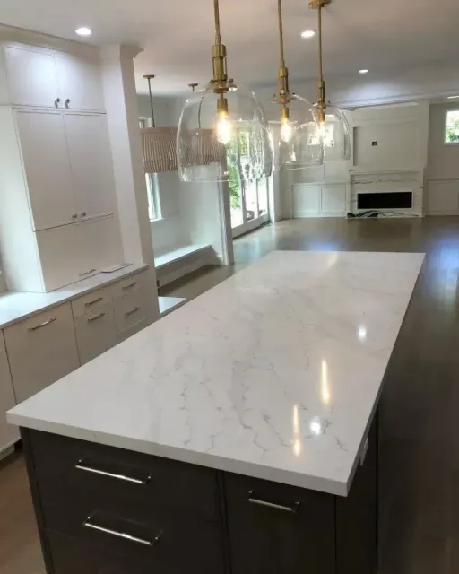 Modern kitchen with a large marble island, pendant lights, white cabinets, and a built-in fireplace