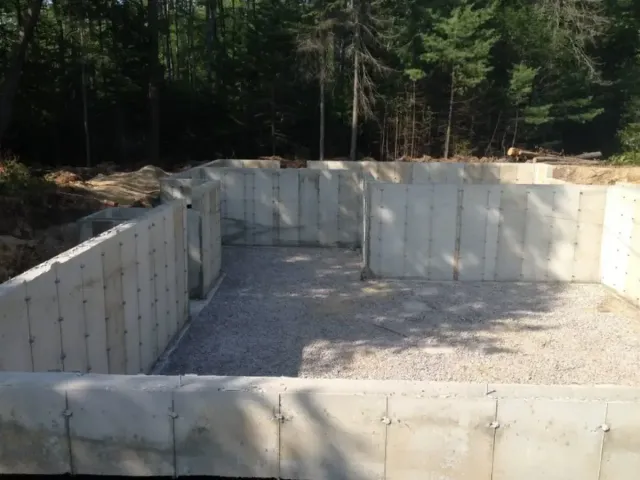 A large concrete wall is surrounded by gravel and trees.