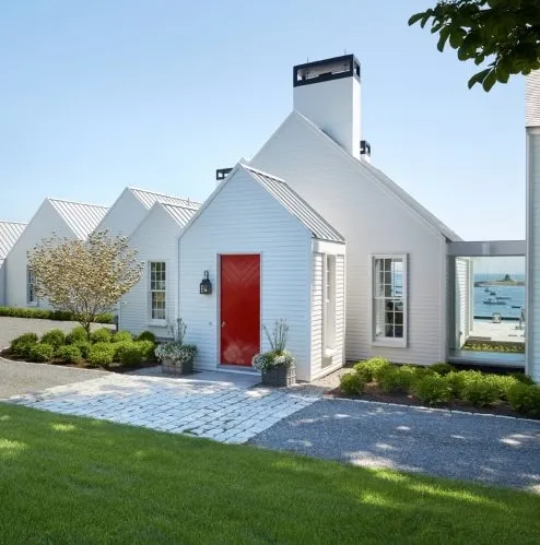 White coastal home with bright red door, lush lawn, and ocean view.