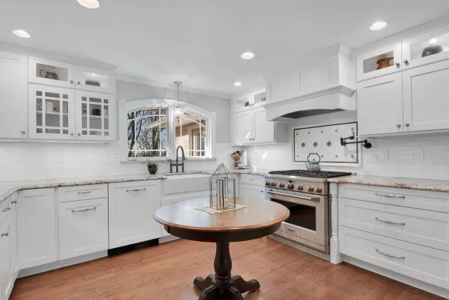 White kitchen with granite countertops, wooden floor, and a round wooden table.