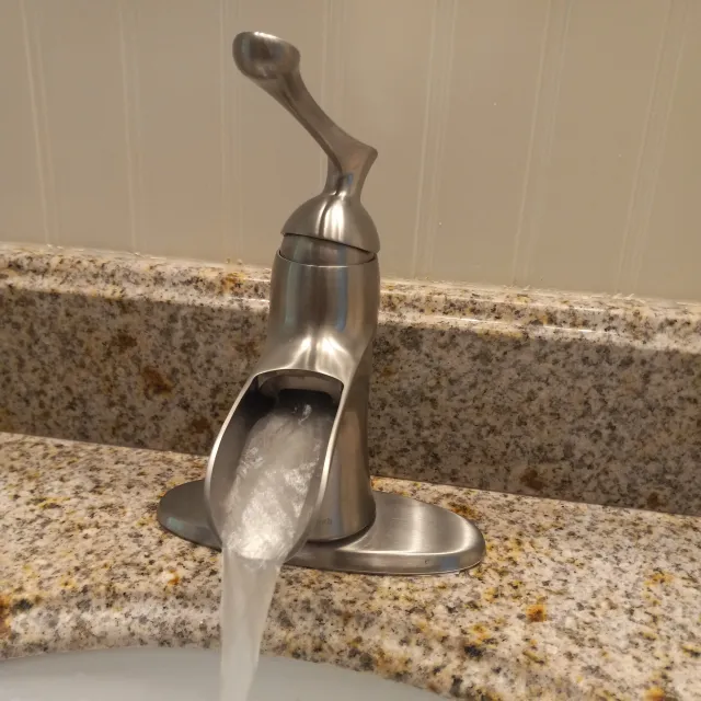 A modern stainless steel faucet with a curved handle, installed on a granite countertop, with water flowing from the spout.