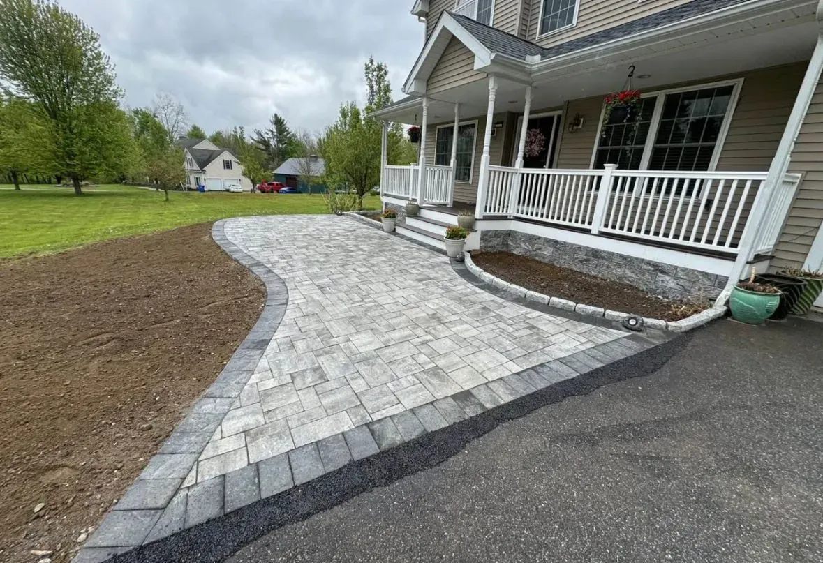 Curved stone walkway beside a white porch and driveway, with a small landscaped mulch bed.