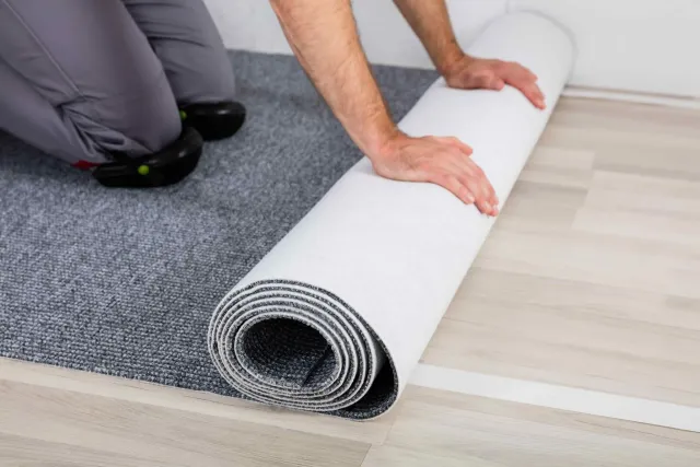 A man is rolling a rug on a wooden floor.