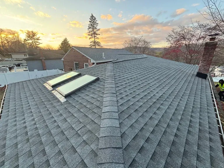 Aerial view of a residential roof with asphalt shingles, ridge vent, and skylights overlooking a lake at sunset