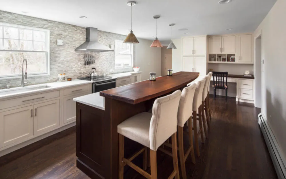 Photo of kitchen with white cabinets, dark floors, island, and pendant lights - Woodland Builders, South Shore MA.