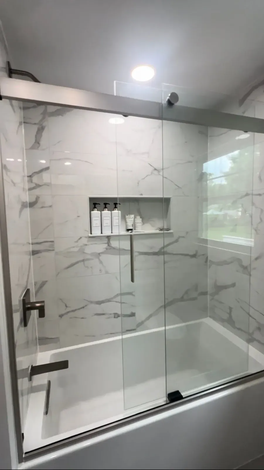 Modern bathroom shower with white marble tile, glass door, and built-in shelves