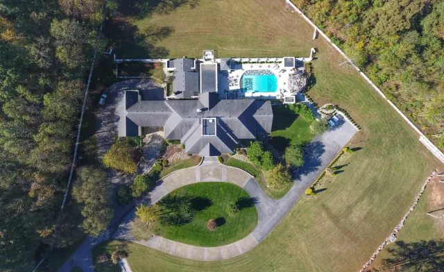 Aerial view of a large house with a backyard pool, surrounded by a spacious lawn and trees.