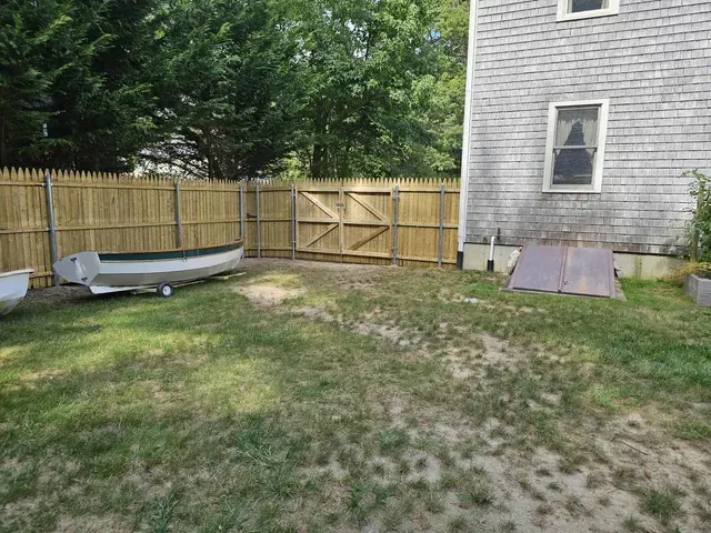 Backyard with wooden fence, small boat on the left, and a house wall with a ramp on the right