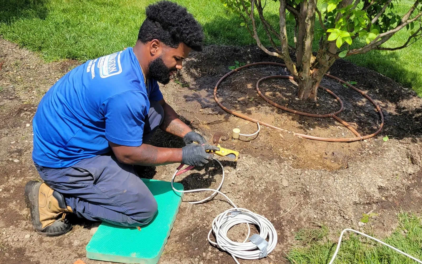 A man in a blue shirt is kneeling down in the dirt.