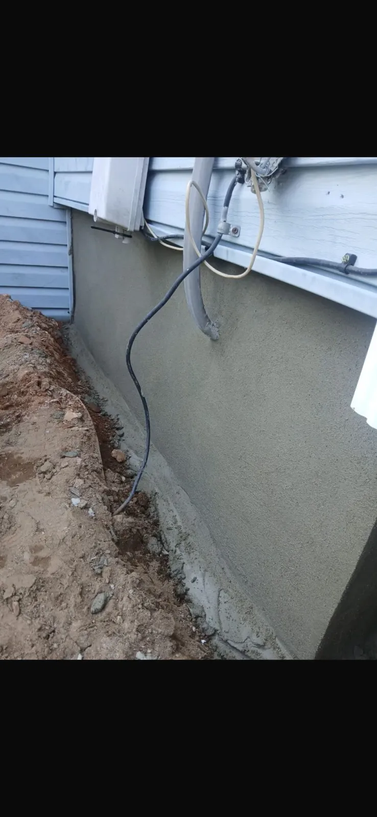 Exterior wall with fresh stucco and dirt alongside. A black wire runs down the wall.