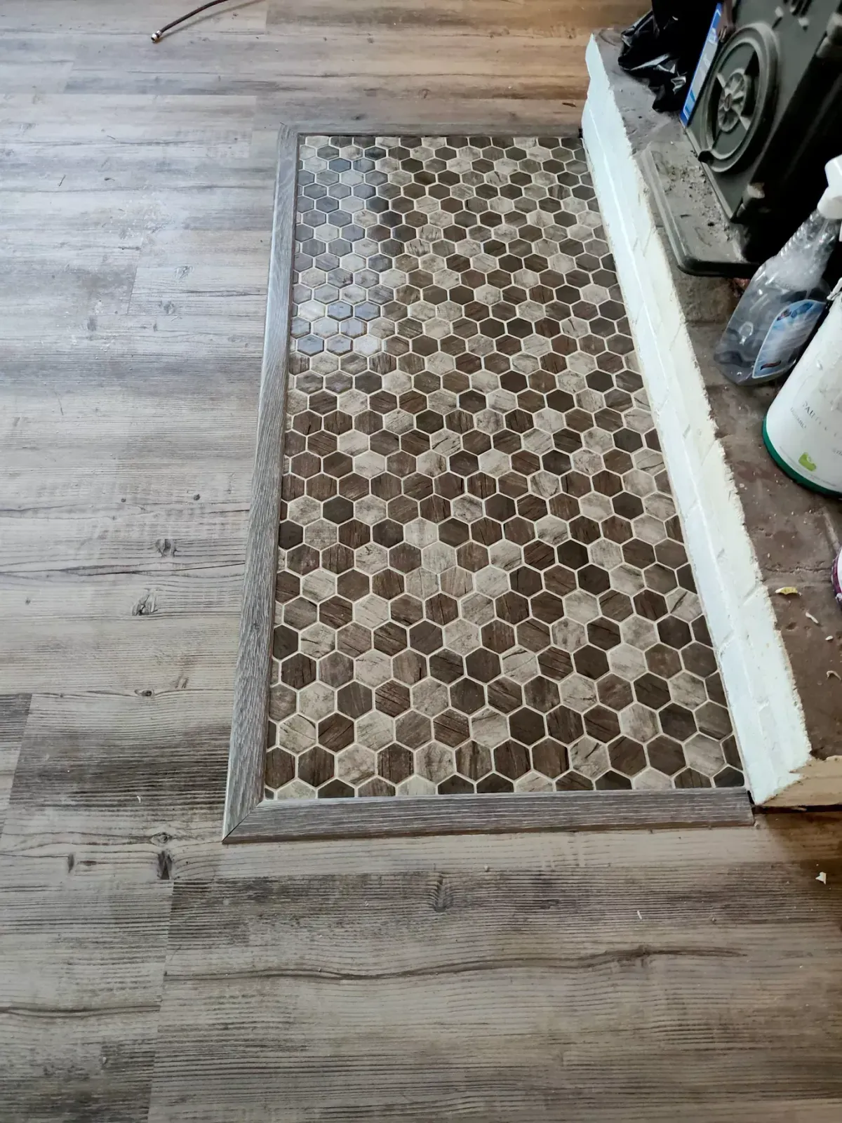 A floor transition showing a mosaic of brown and tan hexagonal tiles bordered by wood-look laminate flooring.