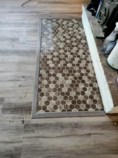 A floor transition showing a mosaic of brown and tan hexagonal tiles bordered by wood-look laminate flooring.