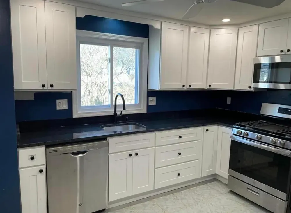 White kitchen cabinets, dark countertops, blue backsplash, stainless steel appliances.