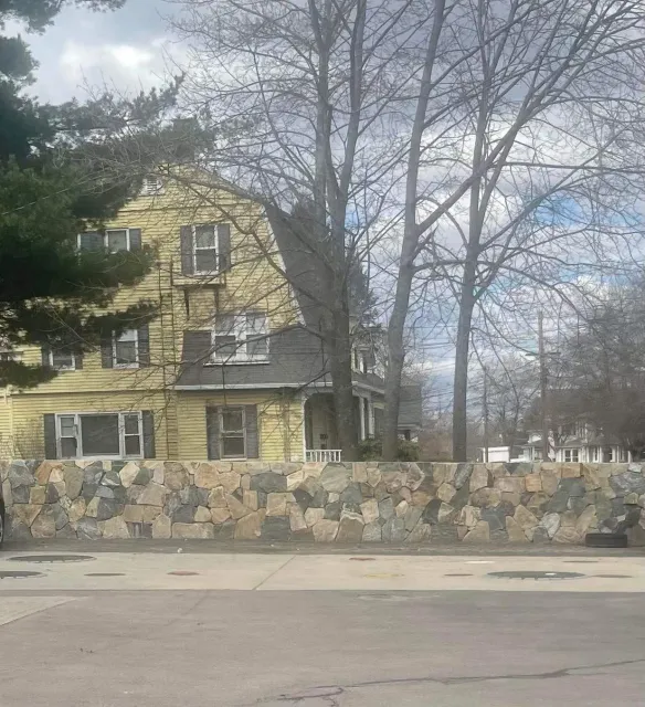 Leafless trees and a yellow house behind a stone wall on a quiet street.