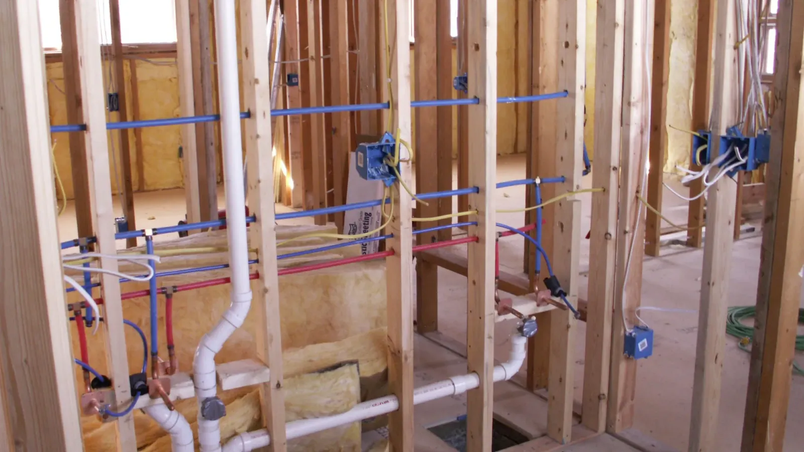 Interior view of wooden studs with exposed plumbing and electrical wiring in a construction setting.