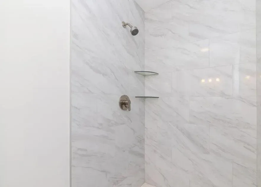 A bathroom with a walk in shower with marble tiles and shelves.