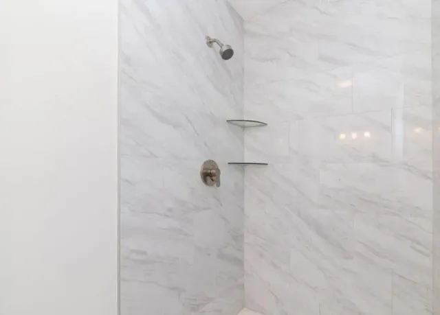 A bathroom with a walk in shower with marble tiles and shelves.