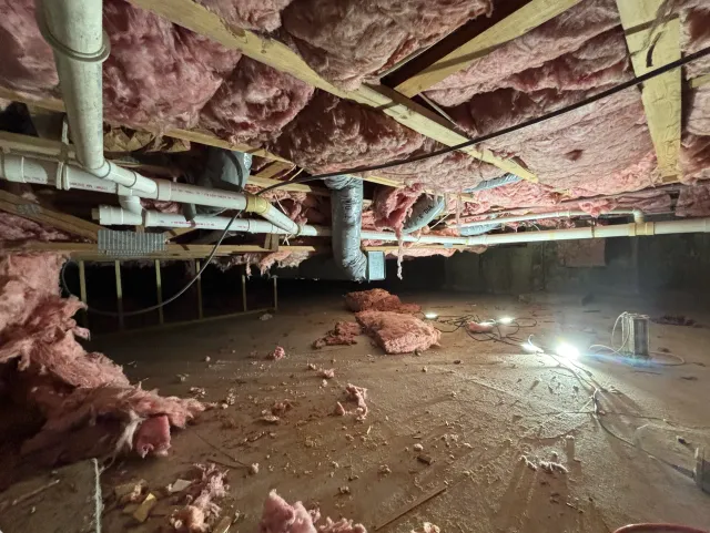 Unfinished basement crawl space with exposed pipes, insulation, and bare concrete