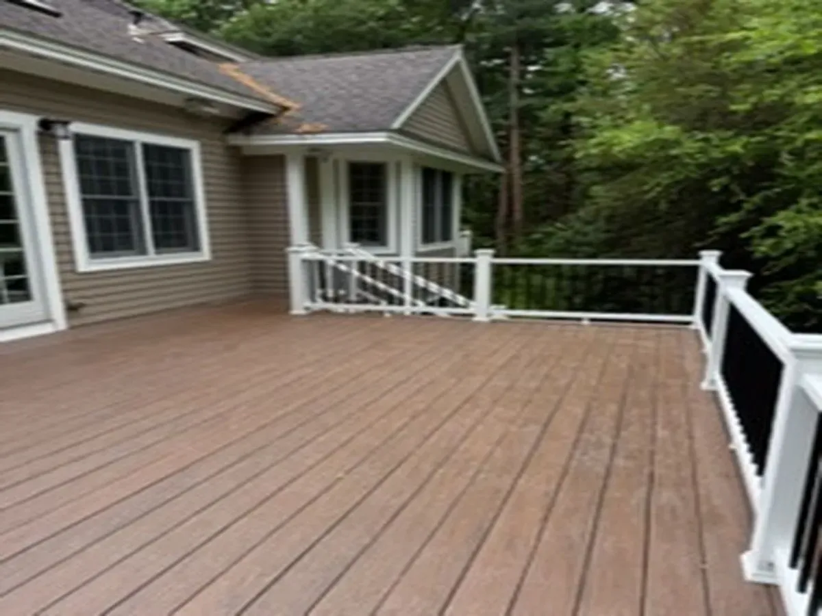 Wooden deck with white railing beside a house, surrounded by trees