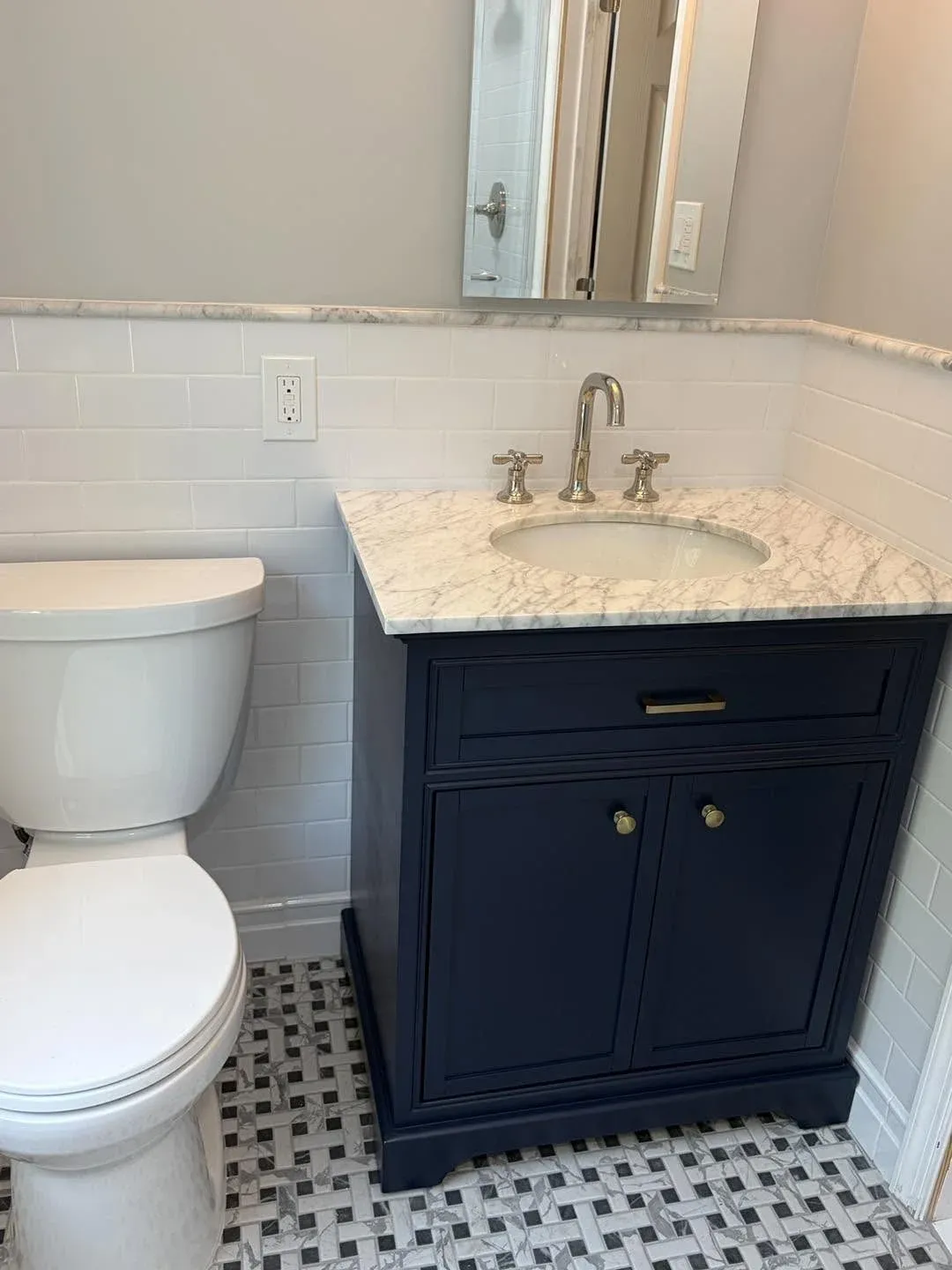 Bathroom vanity close-up showing navy cabinet, marble countertop, cross-handle faucet, and basket-weave tile floor
