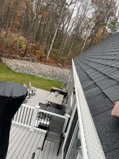 Backyard deck with white railing, black roof, patio furniture, and autumn trees beyond a rock border.