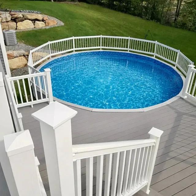Round above-ground pool with blue water, white railing, and gray deck in a grassy backyard