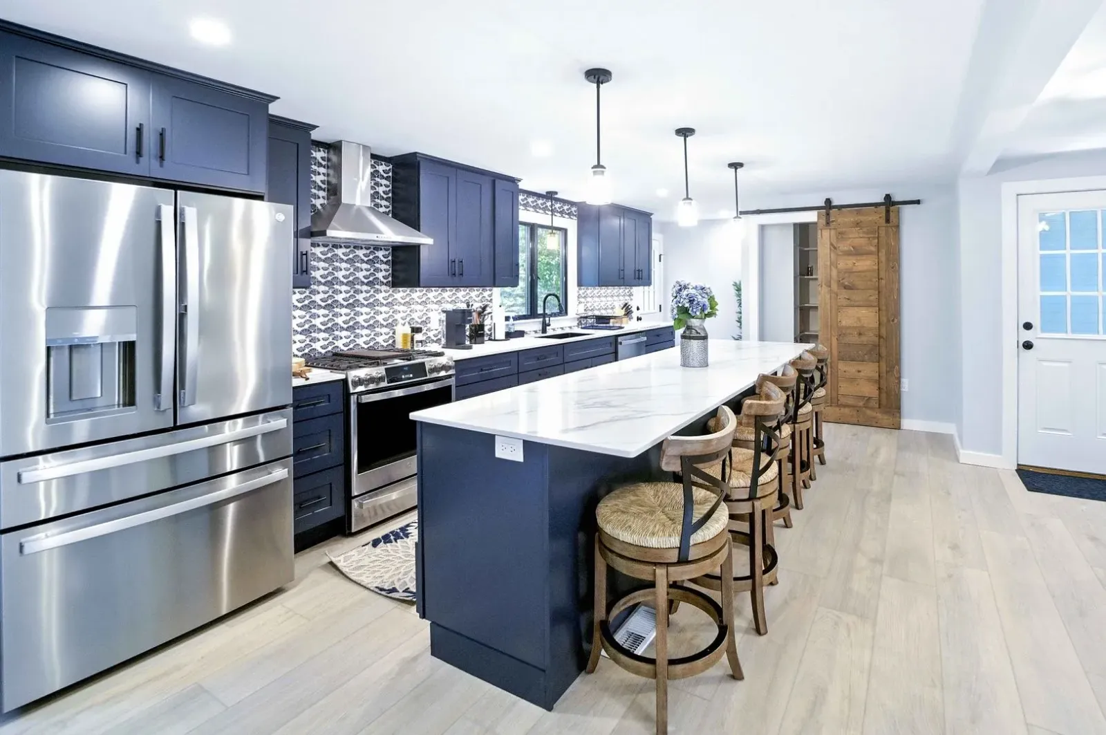 Bright modern kitchen with stainless steel appliances, island, bar stools, and light wood floors.